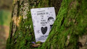 The Danish book "Drengen der fik en hunds hjerte" is placed in a tree with green moss spots