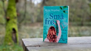 The book Små frø (Small Seeds) by Mette Hegnhøj on a bench in the woods.