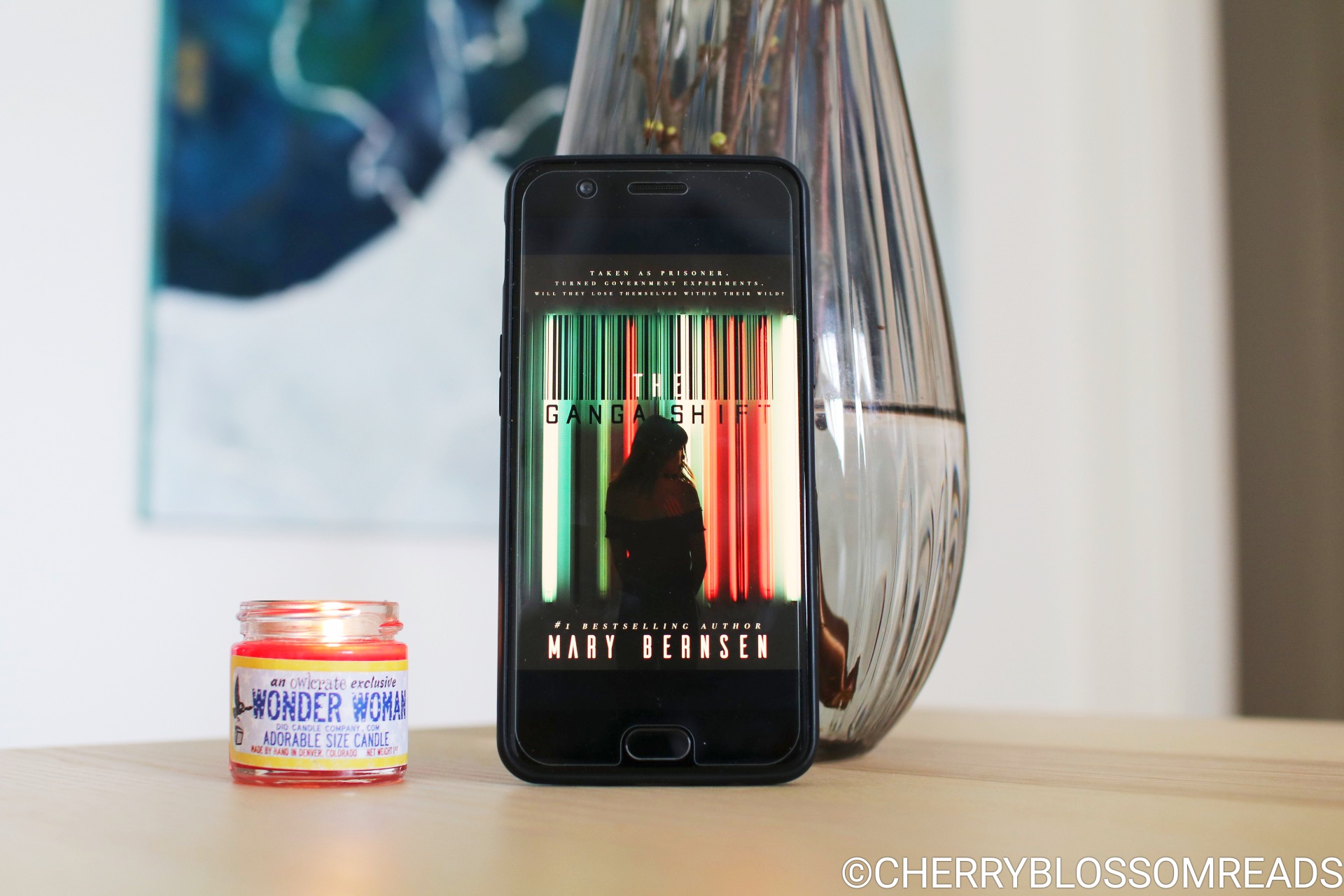 The cover of the e-book The Ganga Shift on a mobile phone next to a grey vase and a read burning candle