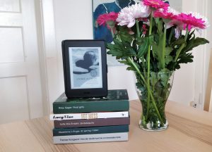 A stack of books I hope to read at Dewey's Readathon next to a vase with pink flowers