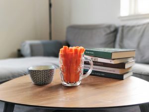 Carrots in a glass and a bowl of hummus on the side. In the background is a book stack