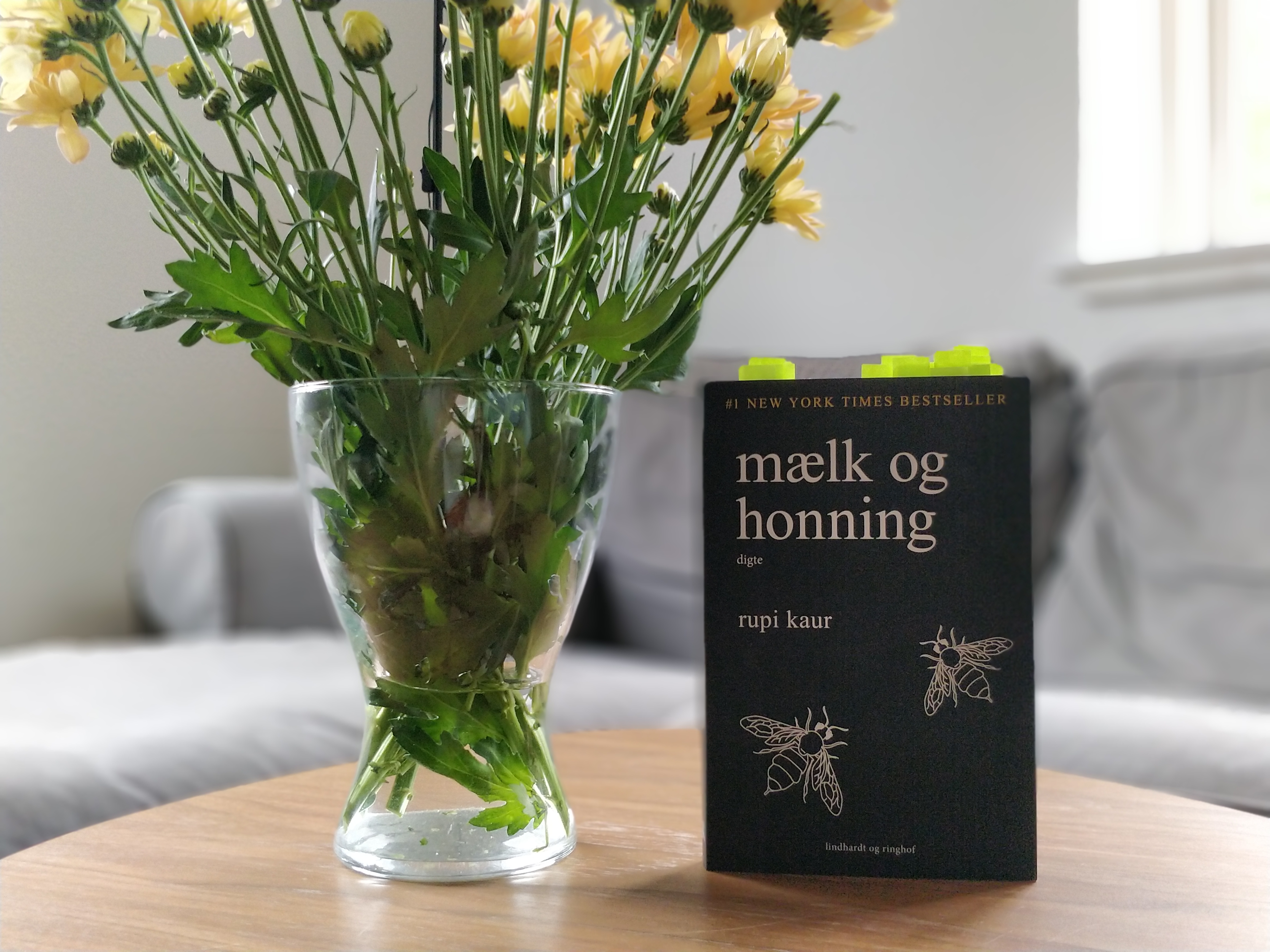 Bogen mælk og honning på et bord ved siden af en vase med gule blomster.