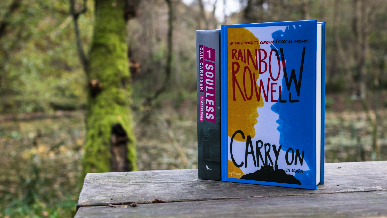 Soulles by Gail Carriger and Carry On by Rainbow Rowell on a bench by a lake